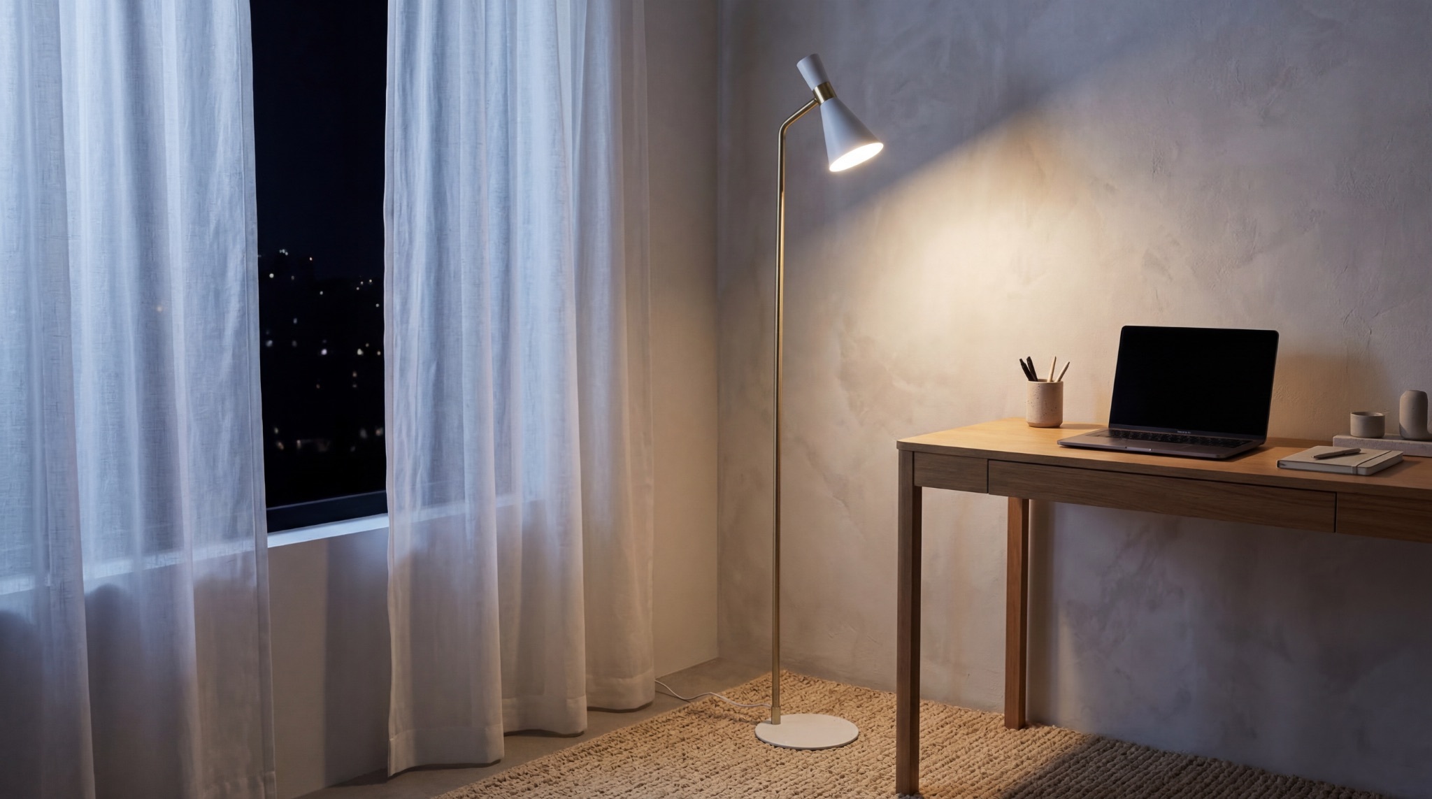 White and brass floor lamp lighting a minimalist home office desk at night